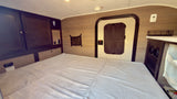 Spacious bed and dark wood cabinets in a clean rv rental interior, with a side door and control panels for comfort.