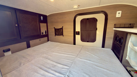 Spacious bed and dark wood cabinets in a clean rv rental interior, with a side door and control panels for comfort.