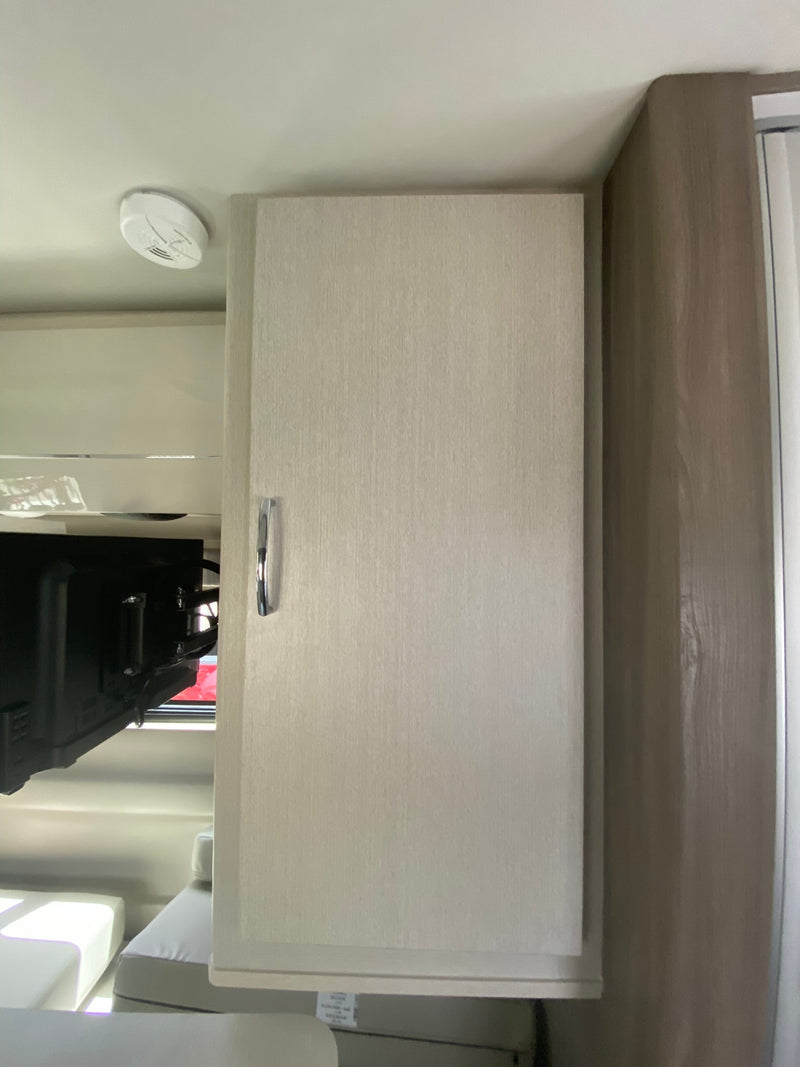 Inside an RV rental: Open cabinet reveals a TV and mount. A smoke detector is visible on the ceiling of this modern interior. — photo 9