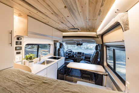 Spacious RV rental camper van interior featuring a bed, compact kitchen, and versatile dining table for comfortable travels.