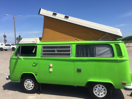 Bright green vintage VW camper van with pop-top, a perfect RV rental for coastal adventures under blue skies.