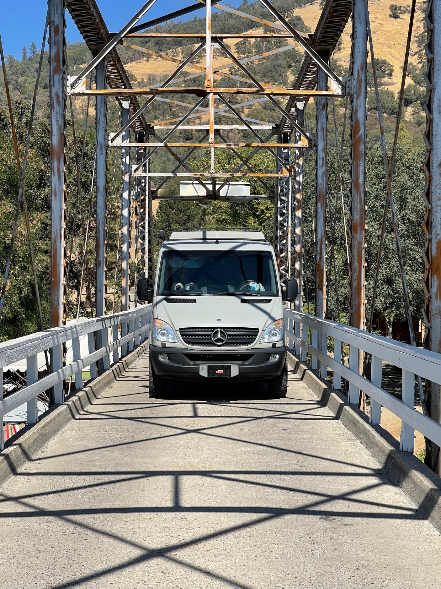 A light gray RV rental van crossing a historic truss bridge, surrounded by scenic hills. Ideal for travel adventures.
