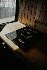 RV rental's functional kitchen: a black true Induction cooktop on a light wood counter, by a window overlooking trees.