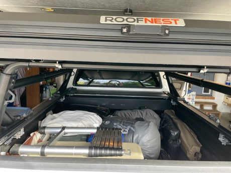 This RV rental-ready truck bed, visible under an open "ROOFNEST" rooftop tent, is packed with overland camping gear.