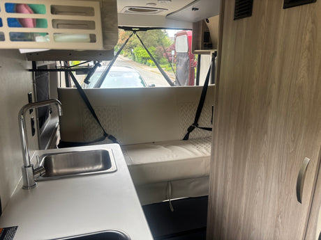 Inside an RV rental: a compact kitchen with sink and faucet, plus a comfy dinette with seatbelts and outdoor views.