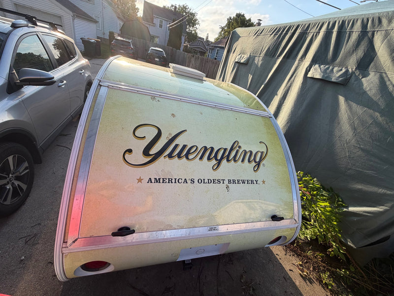  parked in a driveway with attached storage boxes and hitch detail.|A Yuengling beer-branded teardrop trailer — photo 6