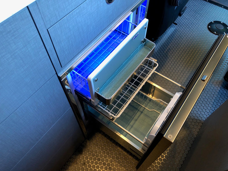 Organized RV rental cooling: a blue-lit Isotherm drawer fridge/freezer with wire baskets opens from textured cabinetry, showing rubber flooring. — photo 8