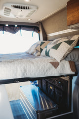 Cozy RV rental interior: elevated bed with quilted bedding, ceiling AC, and practical under-bed storage.