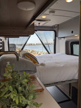 Spacious RV rental interior with a cozy bed & scenic ocean view. Perfect for van life adventures!