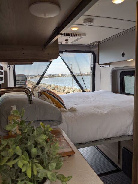 Spacious RV rental interior with a cozy bed & scenic ocean view. Perfect for van life adventures!