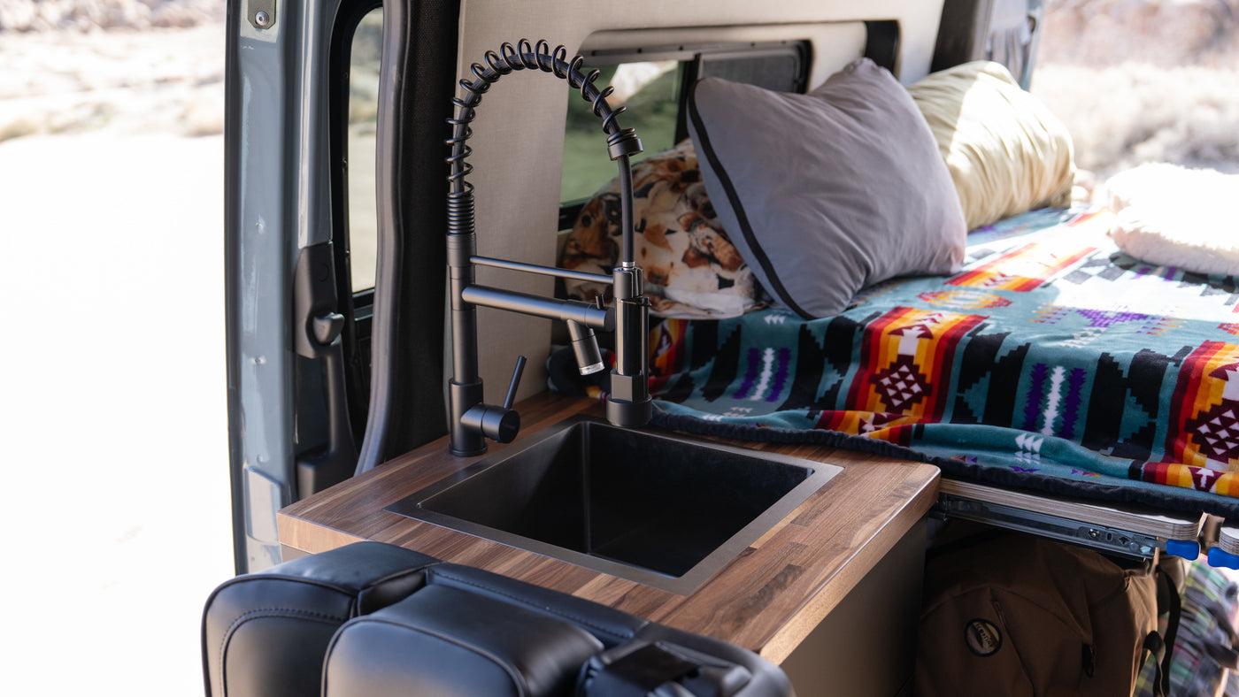 Inside an RV rental: a sleek black sink & wood counter, alongside a cozy bed with colorful blankets, ideal for van life travel. — photo 4