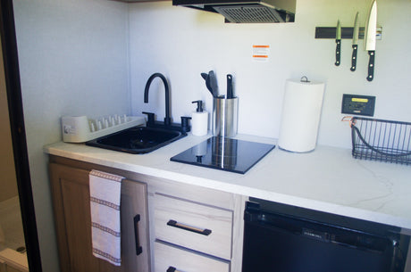 This compact RV rental kitchen features a sink, induction cooktop, refrigerator, and organized cooking essentials.