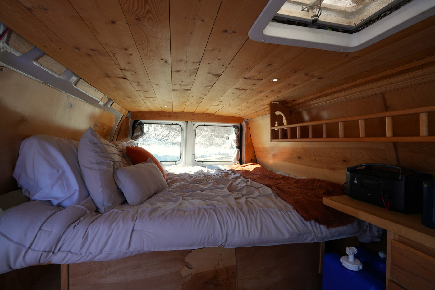 Inside a cozy RV rental: a wooden-paneled camper van bedroom with a comfortable bed, pillows, and snowy window views. — photo 3