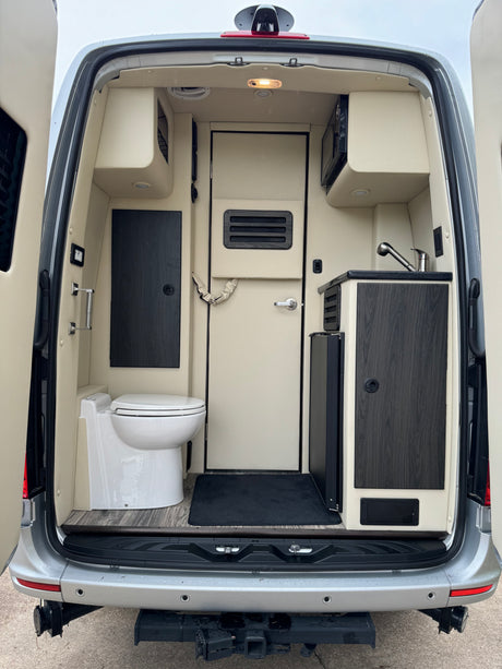 RV rental: Rear view of a spacious camper van interior with a toilet, small kitchen with sink and microwave, and central door.
