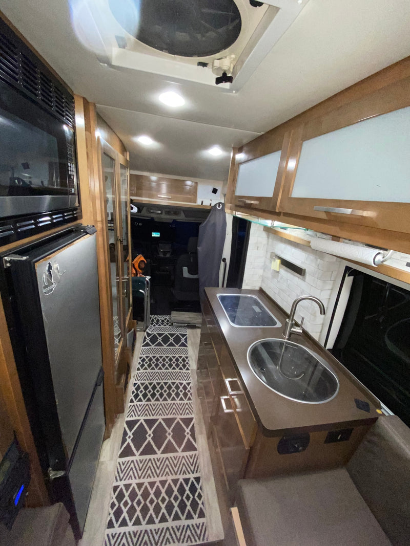 Inside an RV rental: Compact kitchen with sink & stovetop, microwave, fridge, and patterned runner. — photo 10