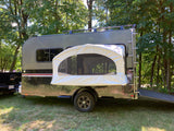A sleek grey RV rental camper with a pop-out tent, roof rack, and ladder, parked in a sunny, tree-filled campsite.