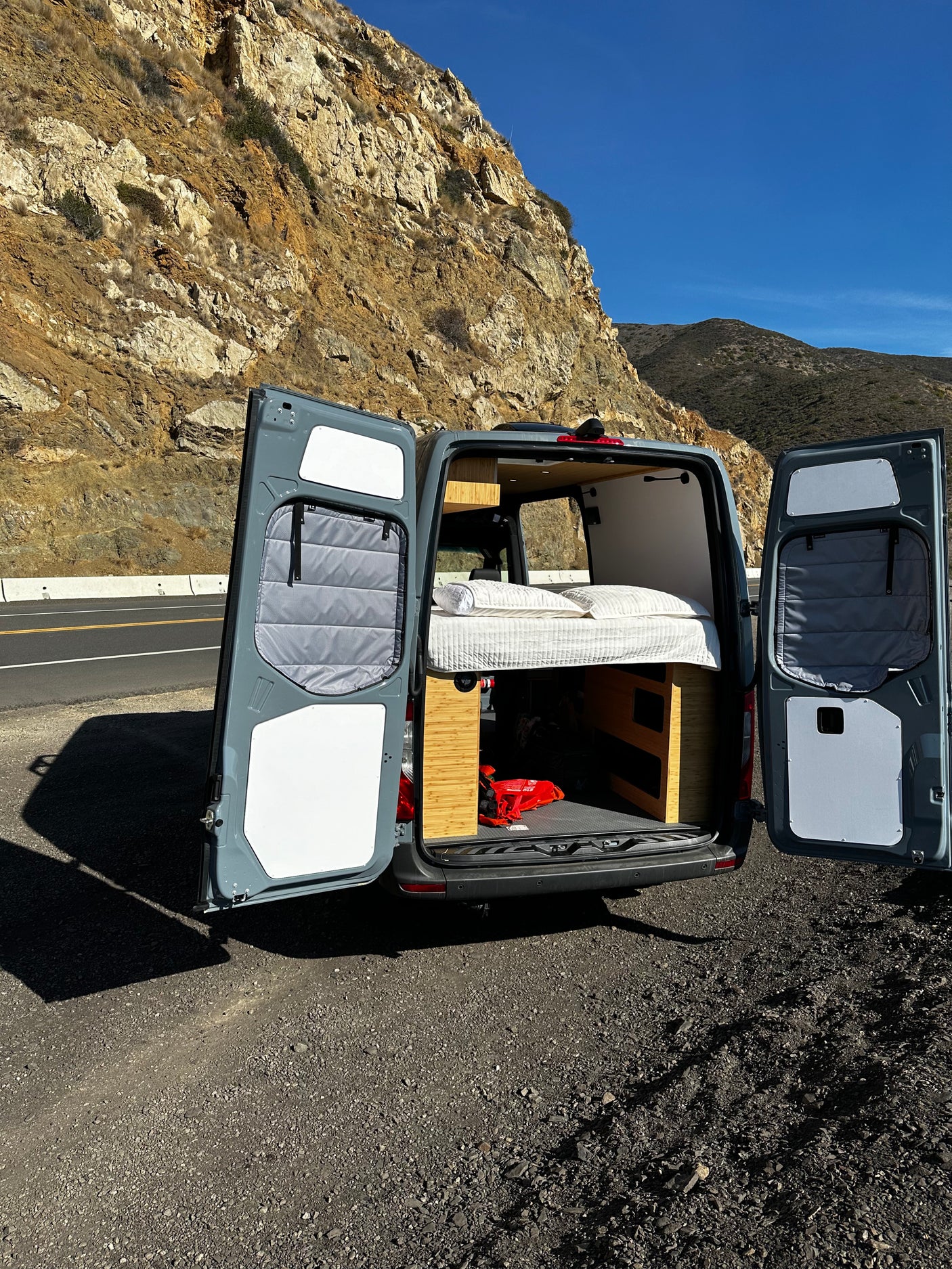 This RV rental van, with its cozy bed revealed, is parked on a scenic mountain road. Perfect for travel adventures!