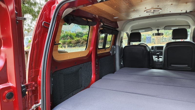 Interior of a red campervan with a large bed, custom wood paneling, and storage nets. An ideal RV rental for adventures. — photo 14