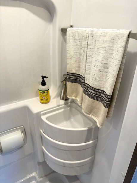Compact RV rental bathroom featuring a corner sink, hand soap, toilet paper holder, and towel bar with a patterned towel.