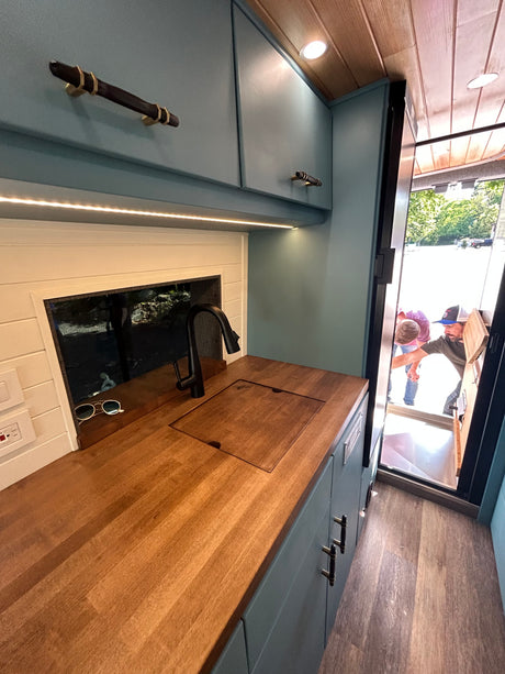 RV rental: Modern van kitchen featuring wood counters, blue cabinets, hidden sink, and bright outdoor entry.