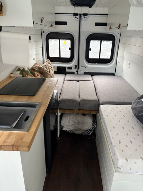 Inside this RV rental, a compact camper van interior featuring a kitchen, flexible bed/seating, and clever storage.
