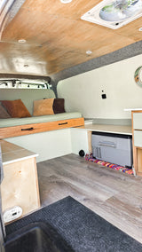 RV rental interior: cozy camper van with bed, built-in storage, wood ceiling, and floor. Includes cooler.