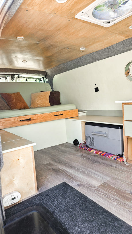 RV rental interior: cozy camper van with bed, built-in storage, wood ceiling, and floor. Includes cooler.