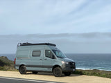 A grey Winnebago Revel 4x4 camper van by scenic ocean, great for an rv rental trip.