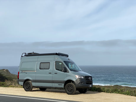 A grey Winnebago Revel 4x4 camper van by scenic ocean, great for an rv rental trip.