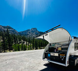 Luna Rover teardrop RV rental with open outdoor kitchen parked by mountains. Ideal for scenic camping trips.
