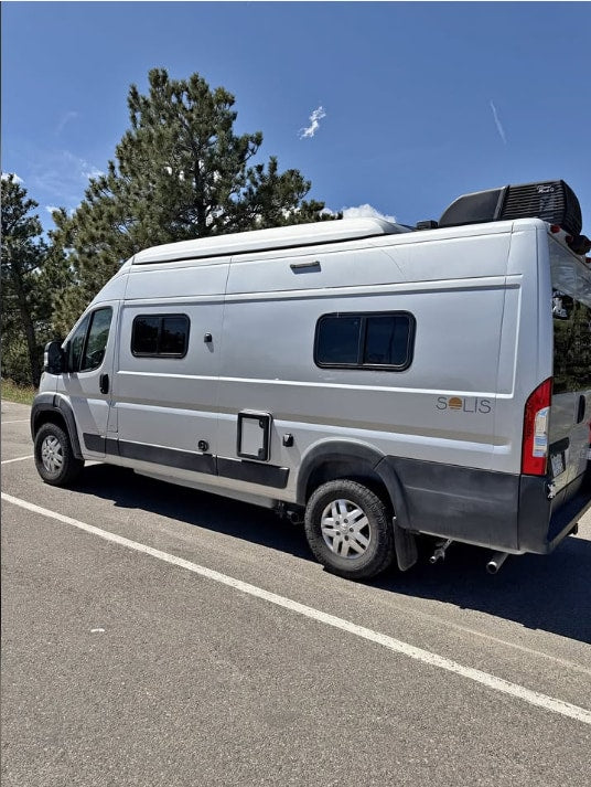 An RV rental, a grey Winnebago Solis camper van, is parked on asphalt with trees and blue sky behind. — photo 16