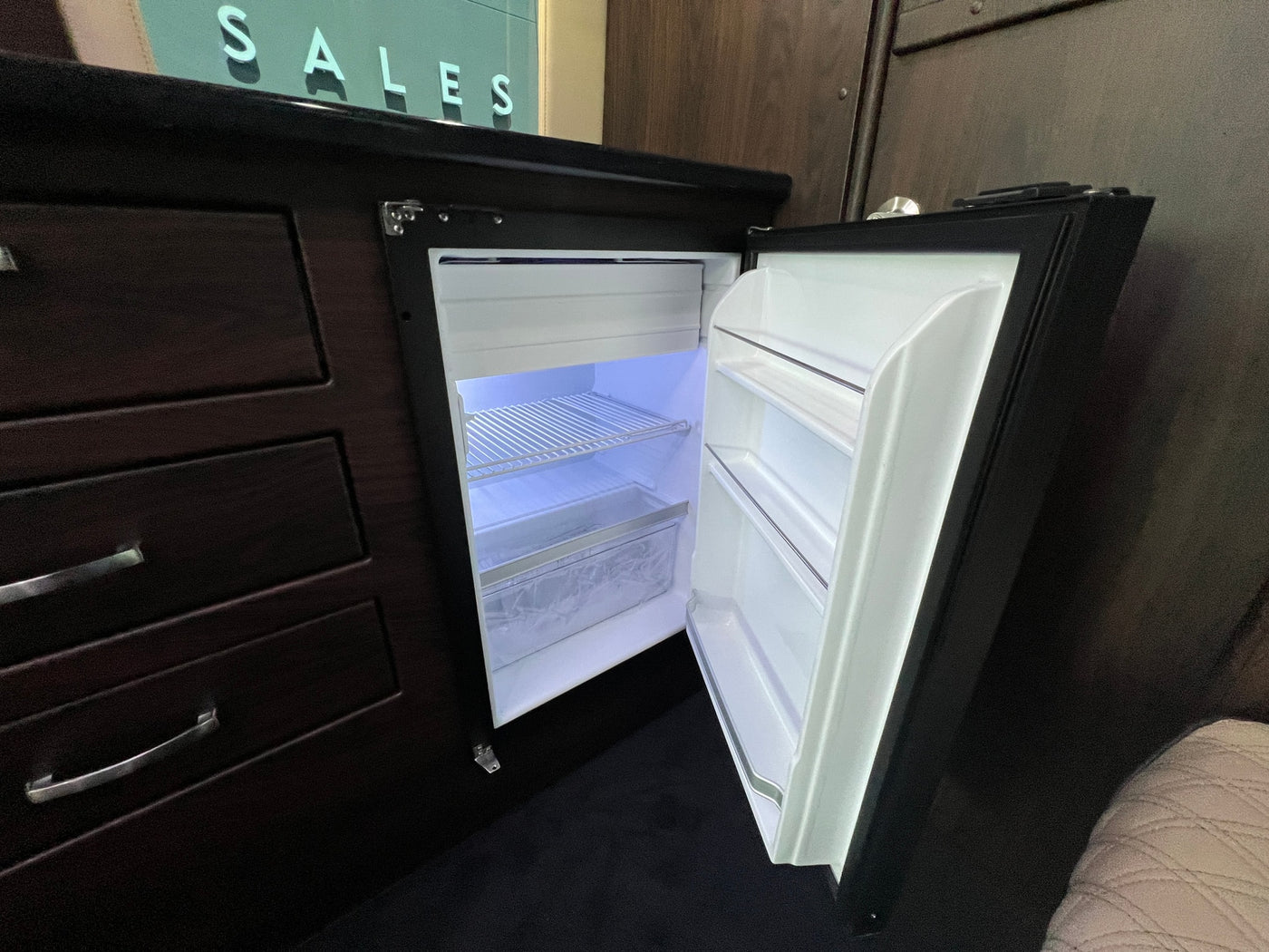 Inside an RV rental: a bright, open mini-fridge built into dark cabinetry alongside storage drawers. — photo 10