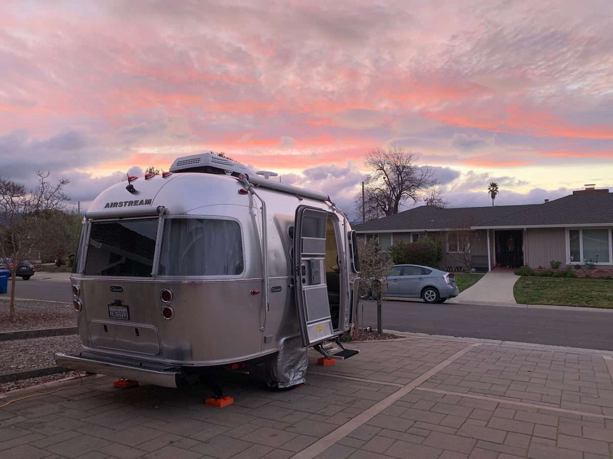 An Airstream RV rental (travel trailer) parked in a residential driveway with a stunning pink and purple sunset overhead.