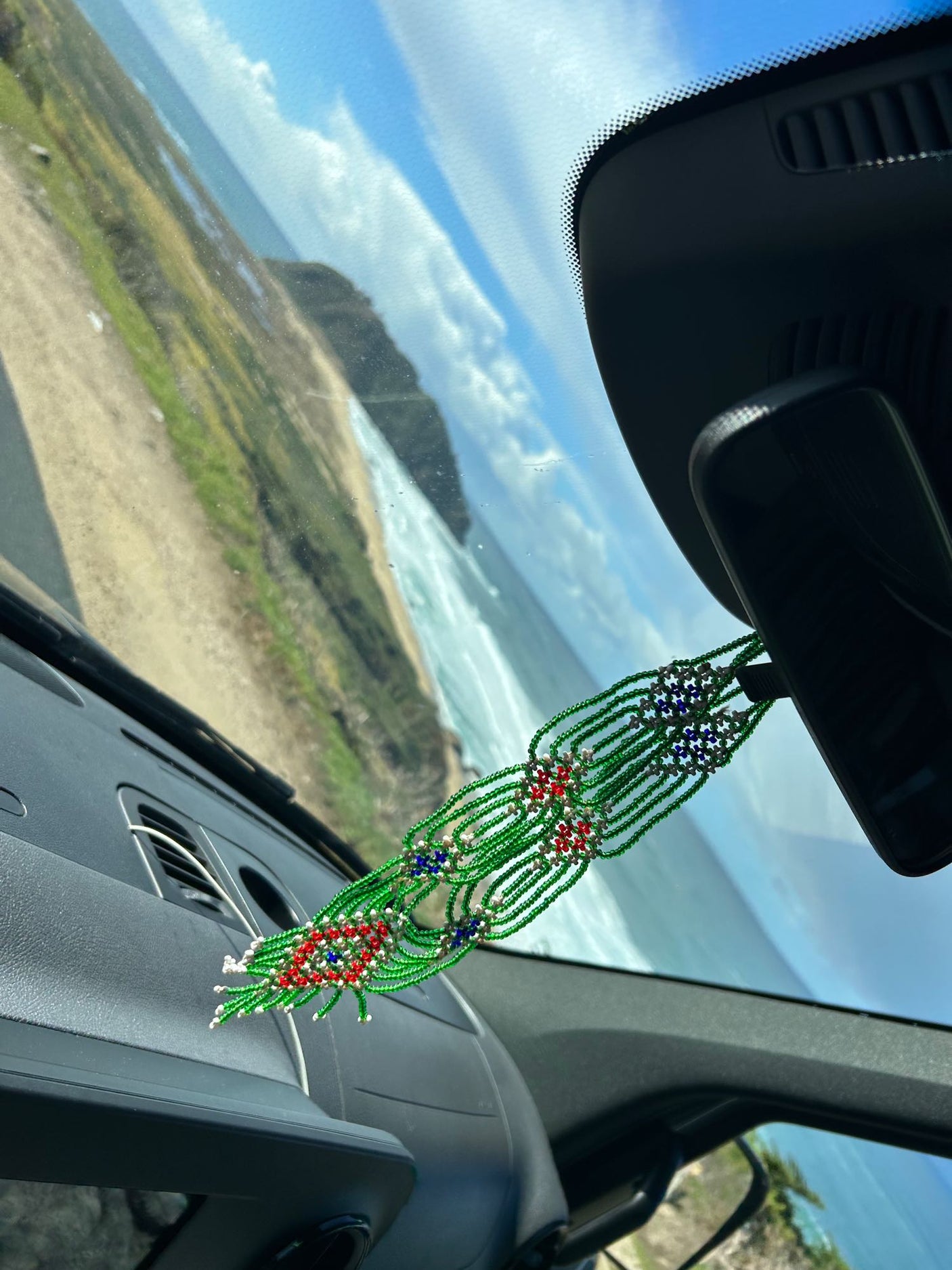 Coastal drive in an rv rental. Beaded car charm overlooks a winding road, cliffs, and ocean.