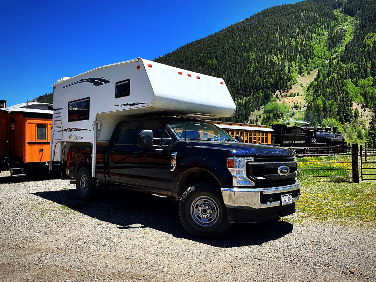  parked near the Durango & Silverton train with a mountain view.|Black Ford truck with a white truck camper (RV) on gravel — photo 3