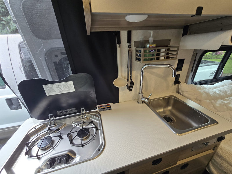 **RV rental** interior: a compact kitchen with a built-in stove and sink, plus white countertops, ideal for on-the-go living. — photo 9