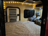 Cozy RV rental interior with a comfortable bed, string lights, and clever storage solutions for your next adventure.