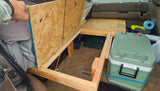 DIY car camping setup in a vehicle's rear. A wooden bed platform with storage, cooler, and stove offer an efficient rv rental alternative.
