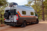 This white Winnebago Solis rv rental, with a spare tire and ladder, rests on a dirt road among pines.
