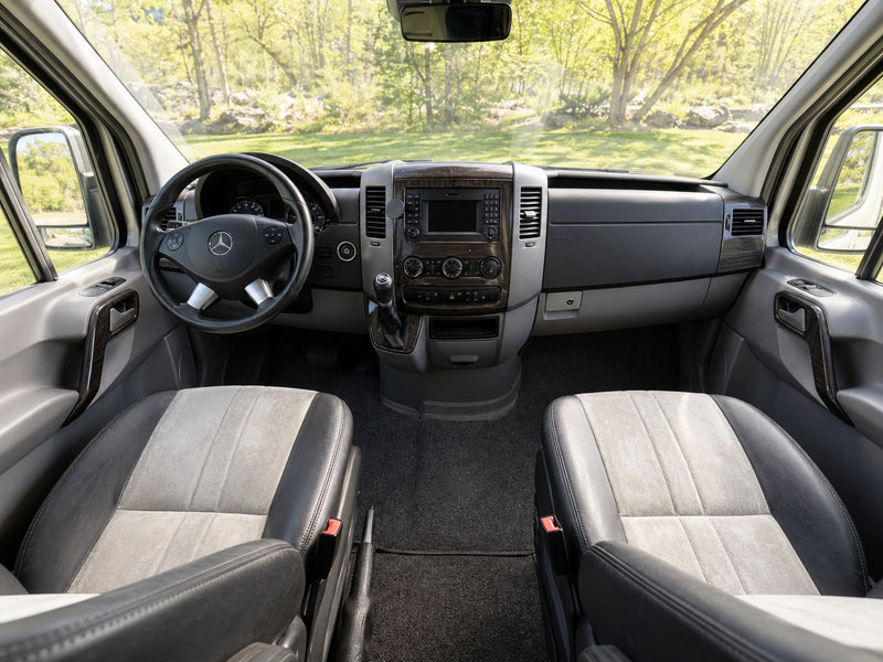 Interior of a Mercedes Sprinter rv rental's front cabin: steering wheel, wood-trimmed dash, & comfy two-tone seats. — photo 6