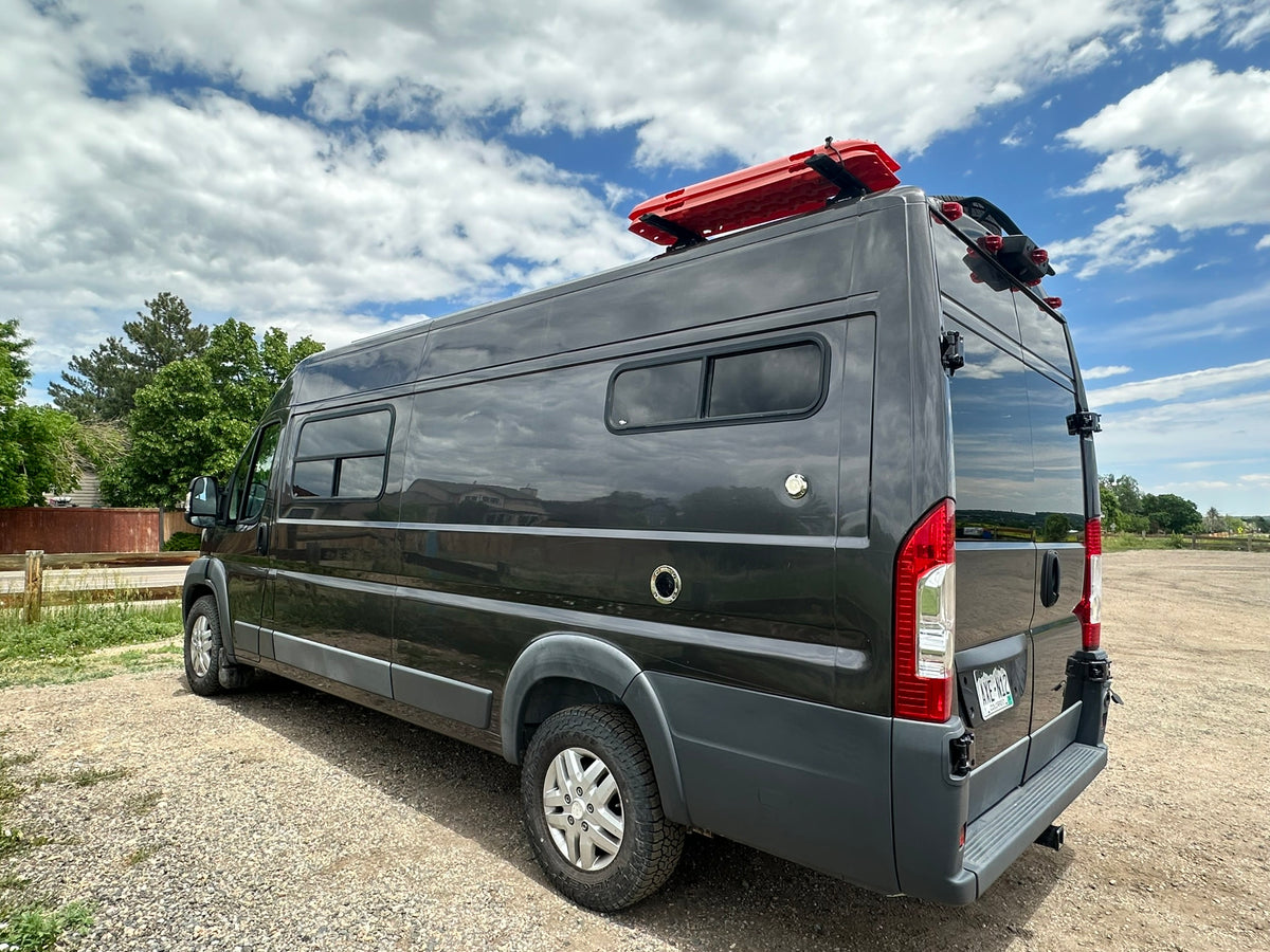Dark gray camper van, equipped with roof recovery boards & rear ladder, ideal for RV rental adventures. Parked on gravel. — photo 19