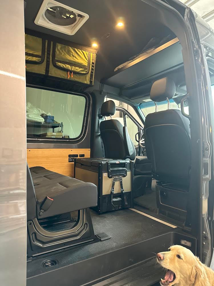 Spacious RV rental interior featuring a fan, storage, portable fridge, and flexible seating. A golden retriever yawns.