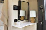 Modern RV rental interior showing a light wood vanity, mirror, woven lamp, and wall-mounted screen. Seatbelt visible.
