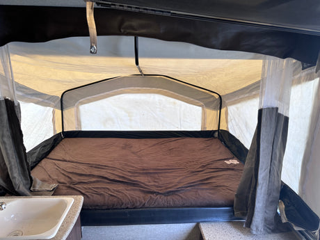 RV rental: Inside a pop-up camper, a large bed with a brown blanket is seen, with a sink and canvas walls on display.