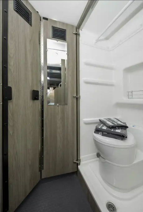 Inside an RV rental: a compact bathroom featuring a folding door with mirror, toilet with towels, and shower area.