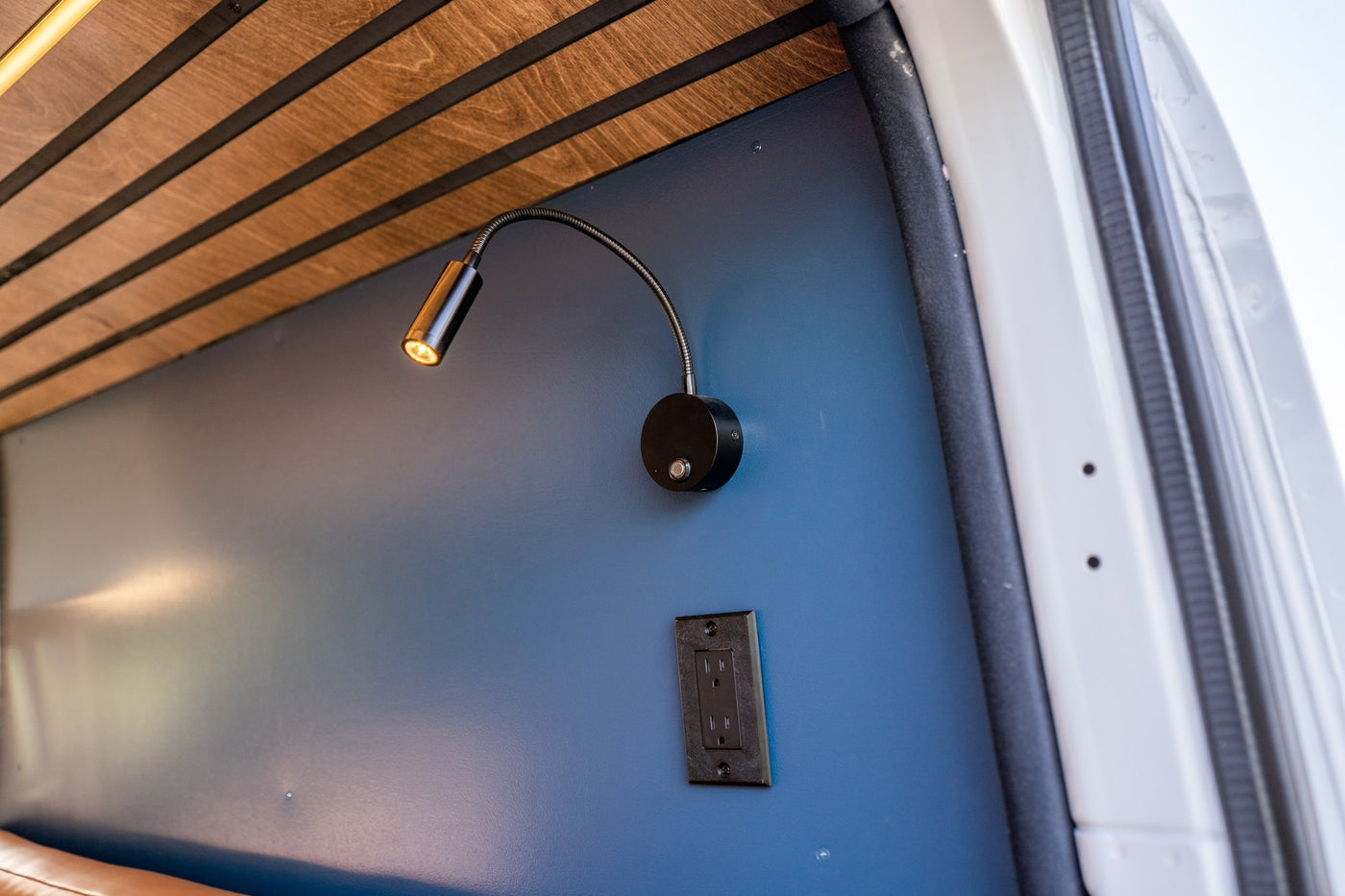 Inside a modern RV rental: sleek wood ceiling, blue wall with a glowing gooseneck light, and a power outlet. — photo 12