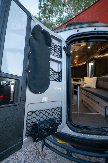 Step inside this RV rental's cozy interior! The open camper door reveals organized storage, comfortable seating, and a table.