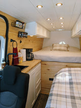 Cozy RV rental interior featuring a compact kitchen with a sink, coffee maker, and a comfortable built-in bed.