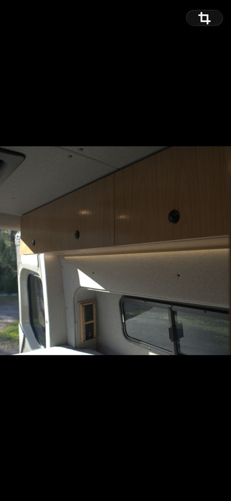 Bright RV rental interior with wooden overhead cabinets, strip lighting, power outlets, & windows.