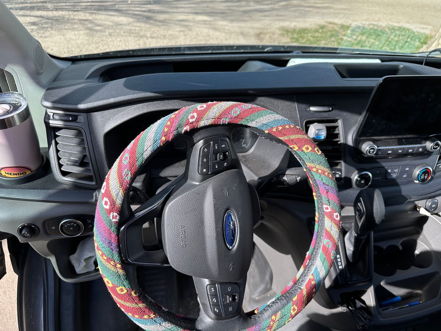 Dashboard of an RV rental, showing a Ford steering wheel with a colorful, patterned cover and a large touchscreen display.
